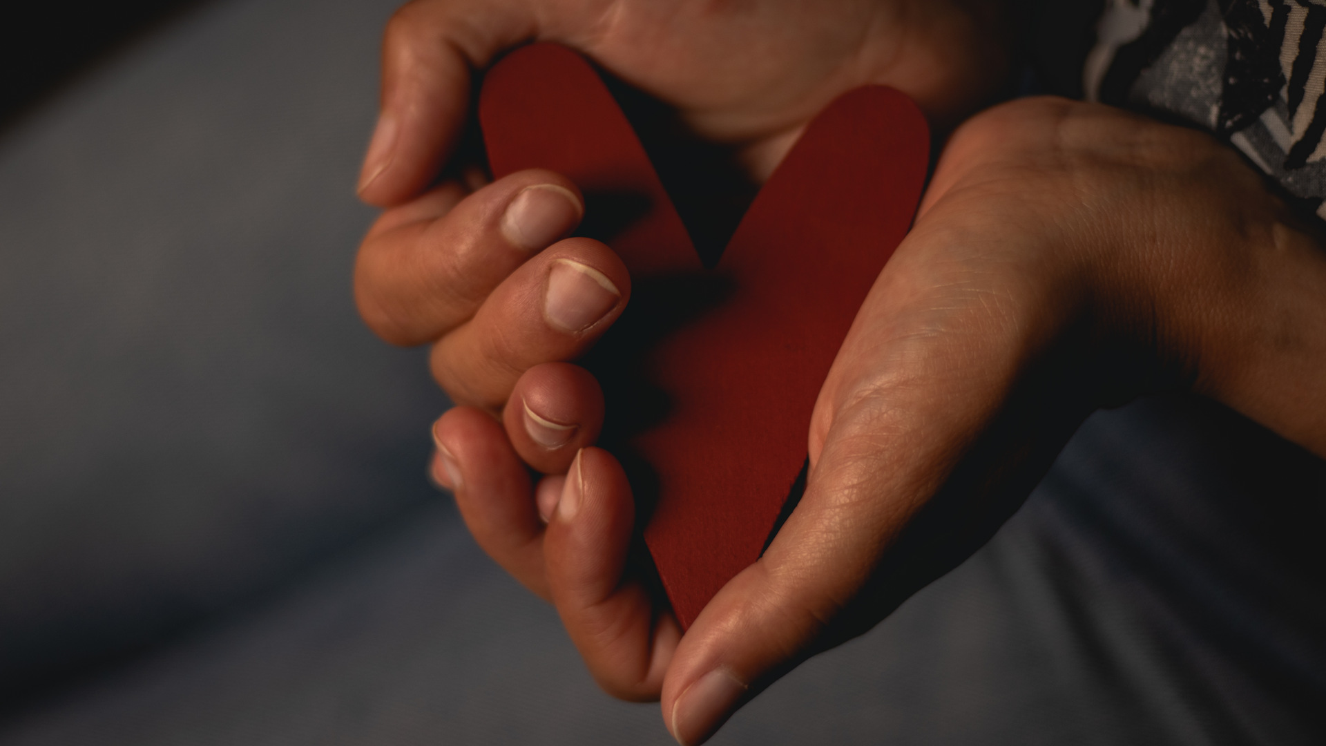 Händer håller i ett rött trähjärta.