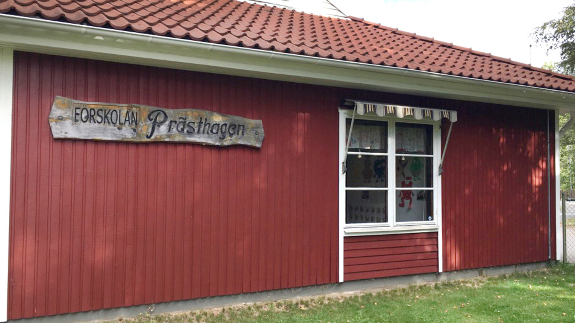 Förskolan Prästhagen som består av ett rött trähus med skylt. Ett vitt fönster med markis är också med i bilden.