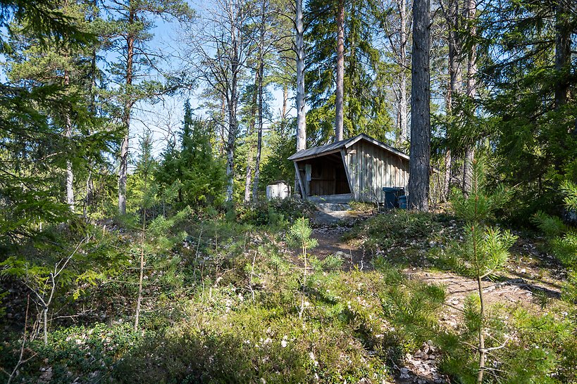 Timrat vindskydd på berg i skog vid sjö.